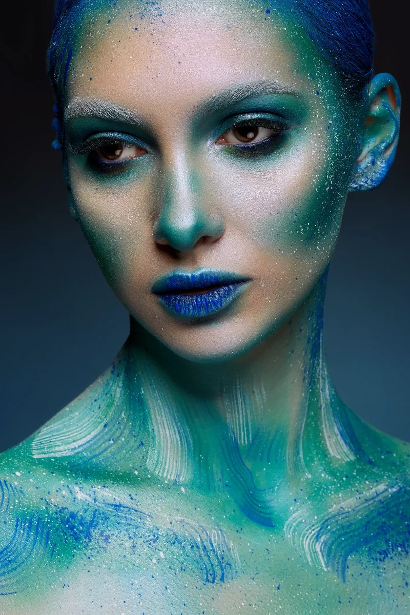 Creative beauty portrait retouching showing a model with blue body paint and speckles of white paint