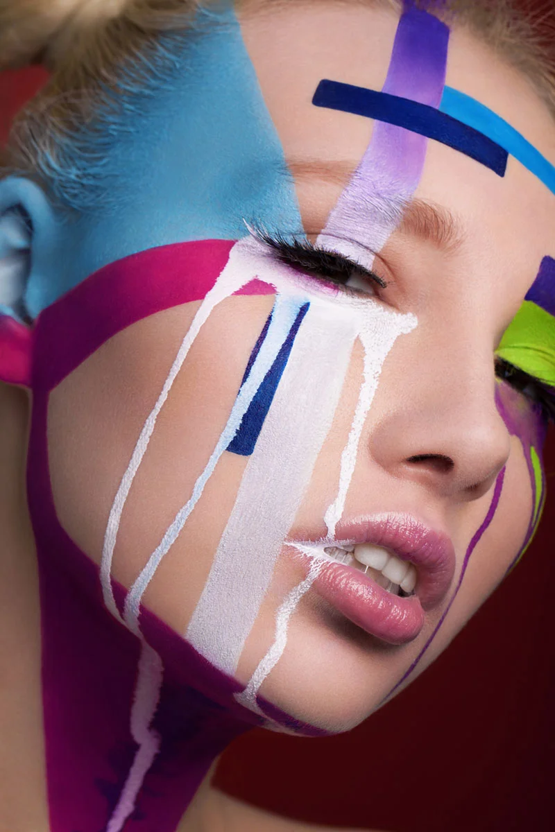 Artistic beauty portrait retouching showing a model with colorful face paint brushstrokes