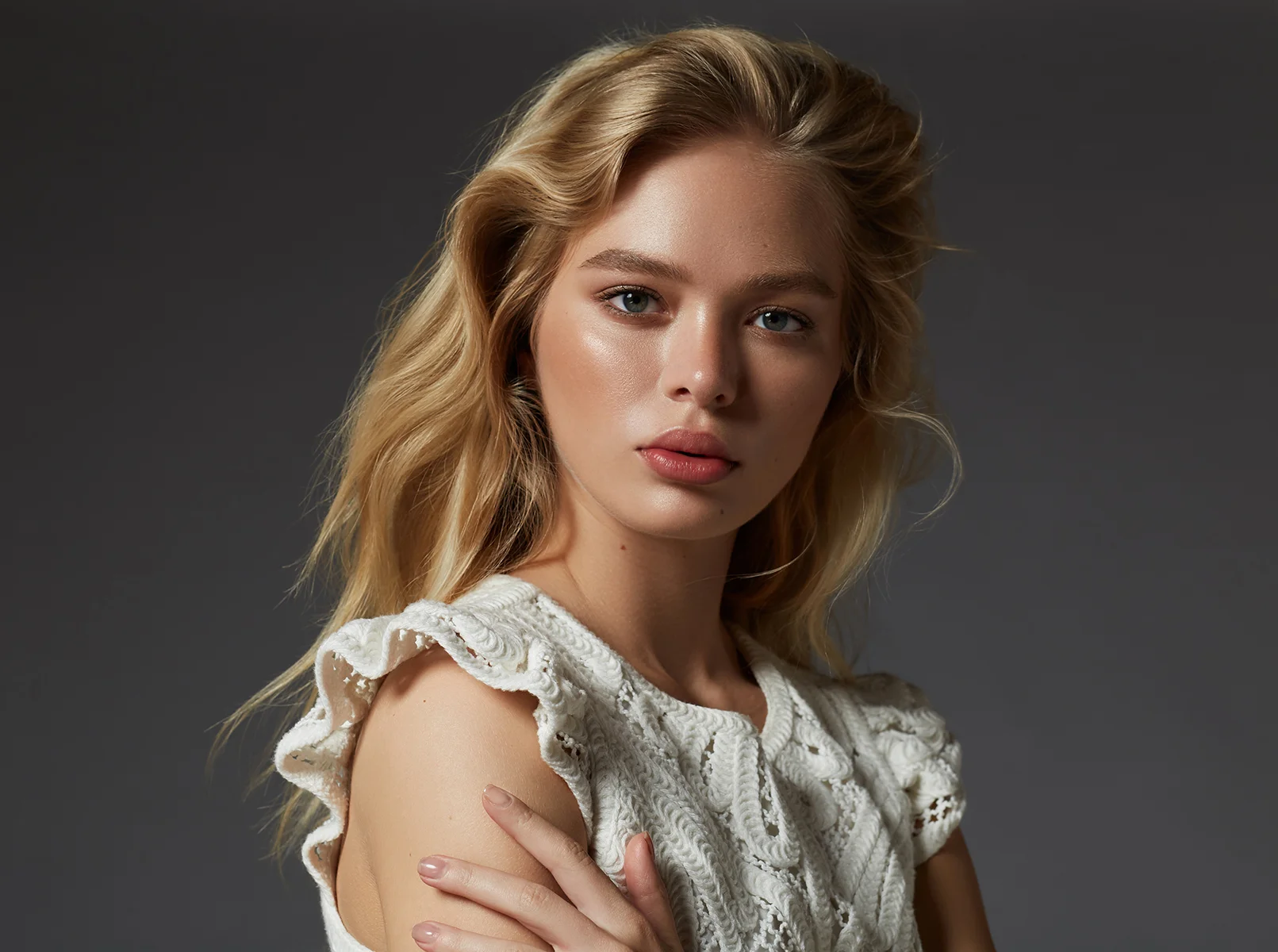 High-end beauty portrait retouching showing a blonde model with flawless glowing skin and soft natural makeup wearing a white lace top
