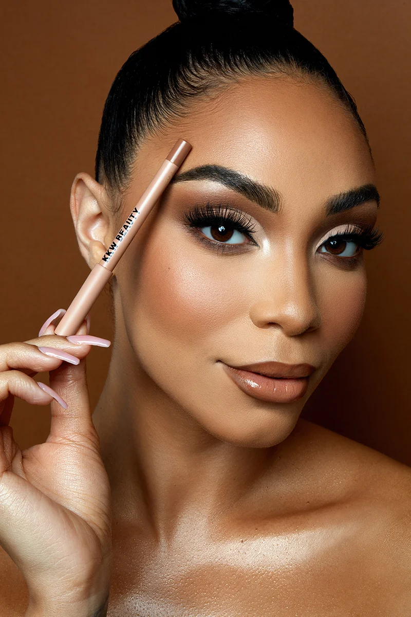 Commercial beauty portrait retouching of a model holding a makeup pencil with glowing skin and warm tone makeup