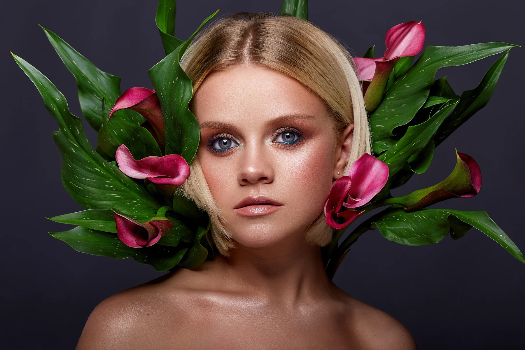Artistic beauty portrait retouching featuring a blonde model with pink calla lilies framing her face and vibrant blue eye makeup