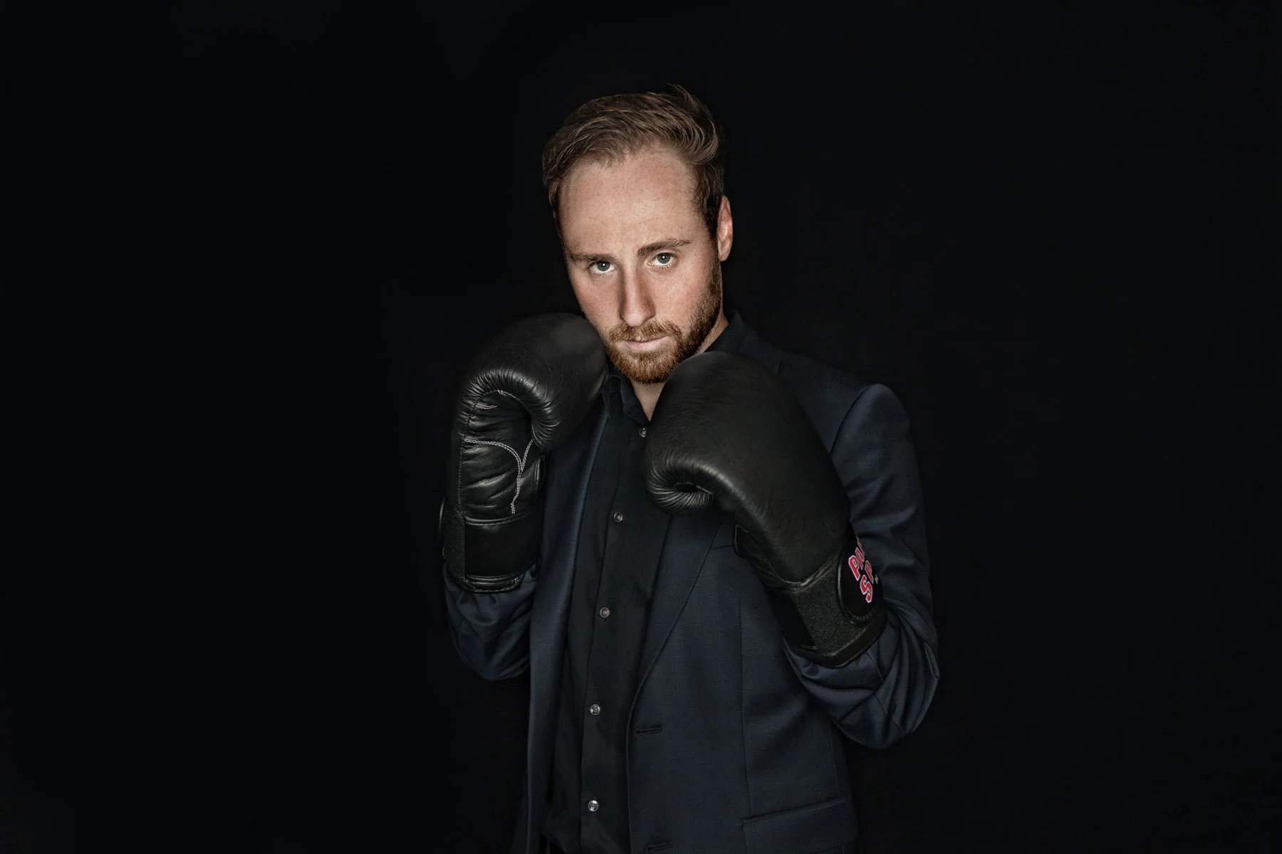 Creative business portrait retouching of a bearded businessman posing in black boxing gloves on a dark background