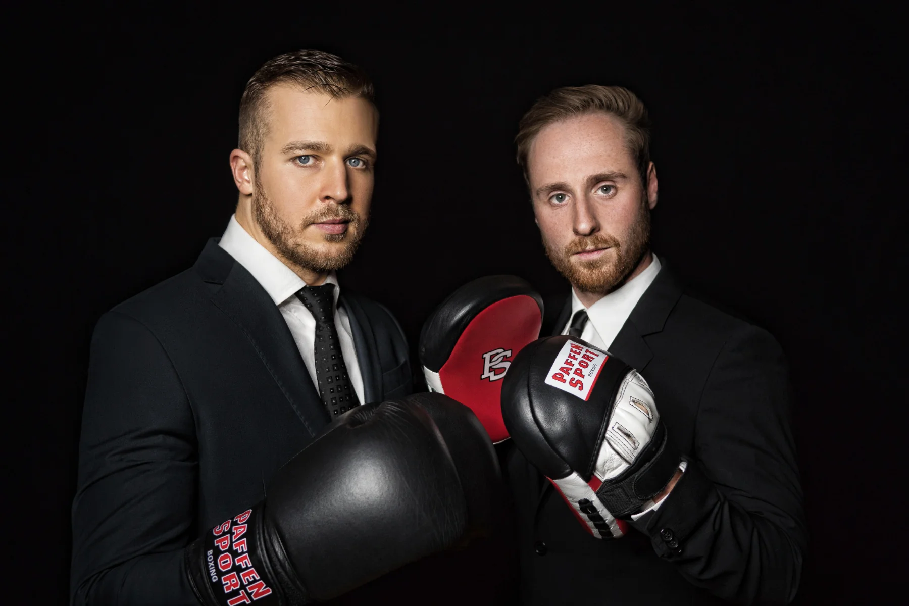Creative corporate portrait retouching of two businessmen in suits with boxing gloves on a black background