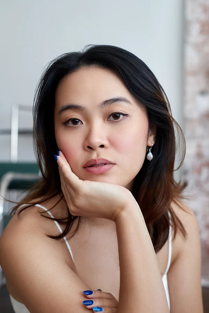 Close-up business portrait retouching of an Asian woman resting her chin on her hand wearing pearl earrings and a white top