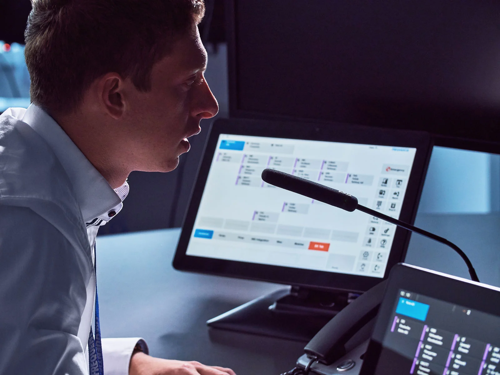 Control room operator portrait retouching showing dispatcher profile speaking into a microphone in front of software dashboard screens