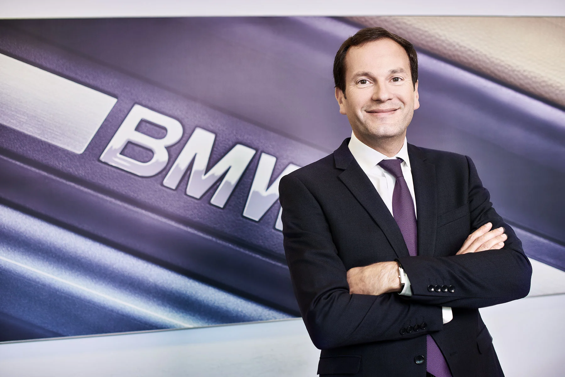 Executive headshot retouching of a confident businessman standing with arms crossed in a corporate office