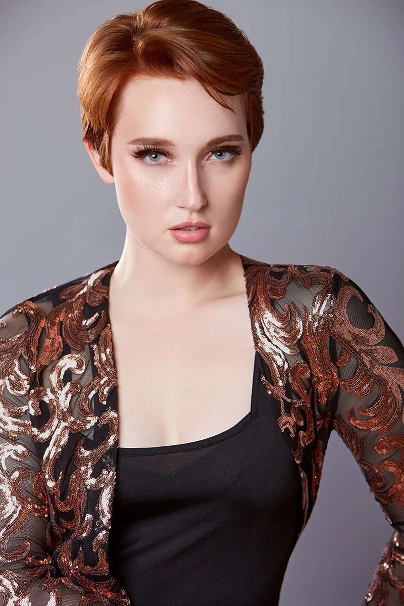 Elegant business portrait retouching showing a redhead woman in a black dress with bronze sequin details