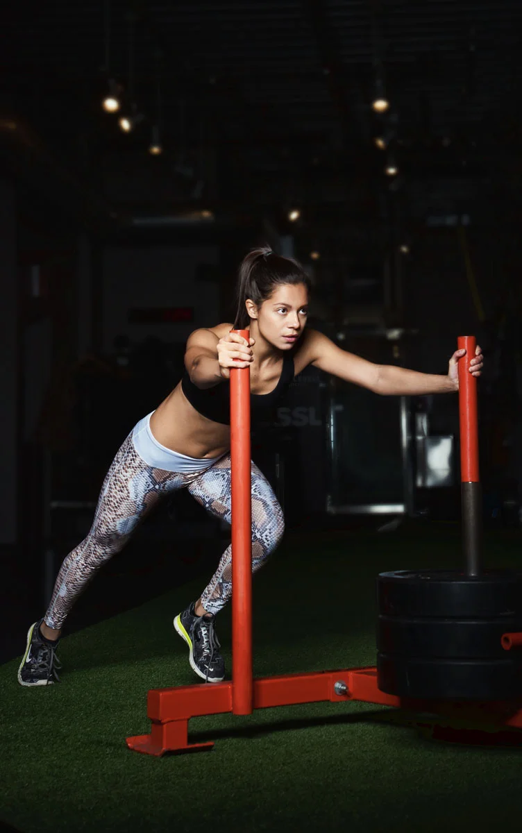 Commercial fitness photography retouching of a female model pushing a weighted sled in a gym environment
