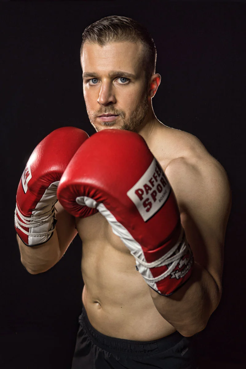 Professional boxer portrait retouching showing male athlete posing in red boxing gloves on a black background
