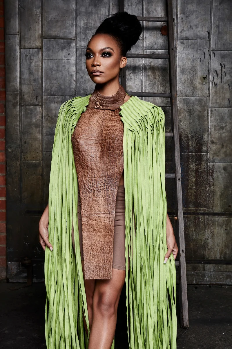 Editorial fashion portrait retouching of a Black model wearing a brown leather dress and a bright green fringed cape