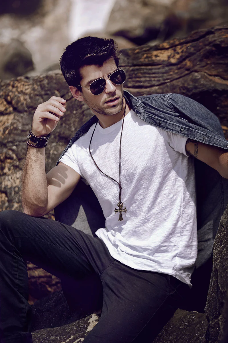 Professional outdoor portrait retouching of a male model wearing sunglasses and a white t-shirt sitting on rocks