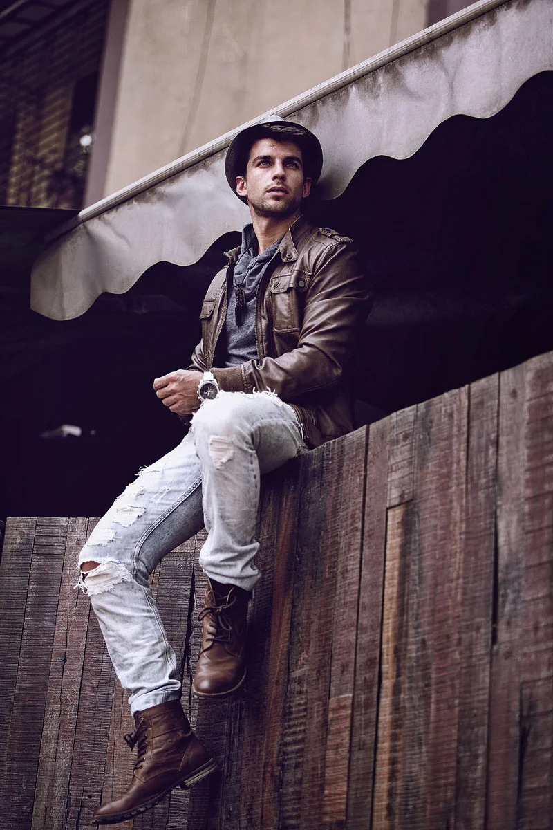 Streetwear fashion photography retouching showing a male model wearing a brown leather jacket and hat sitting on a fence
