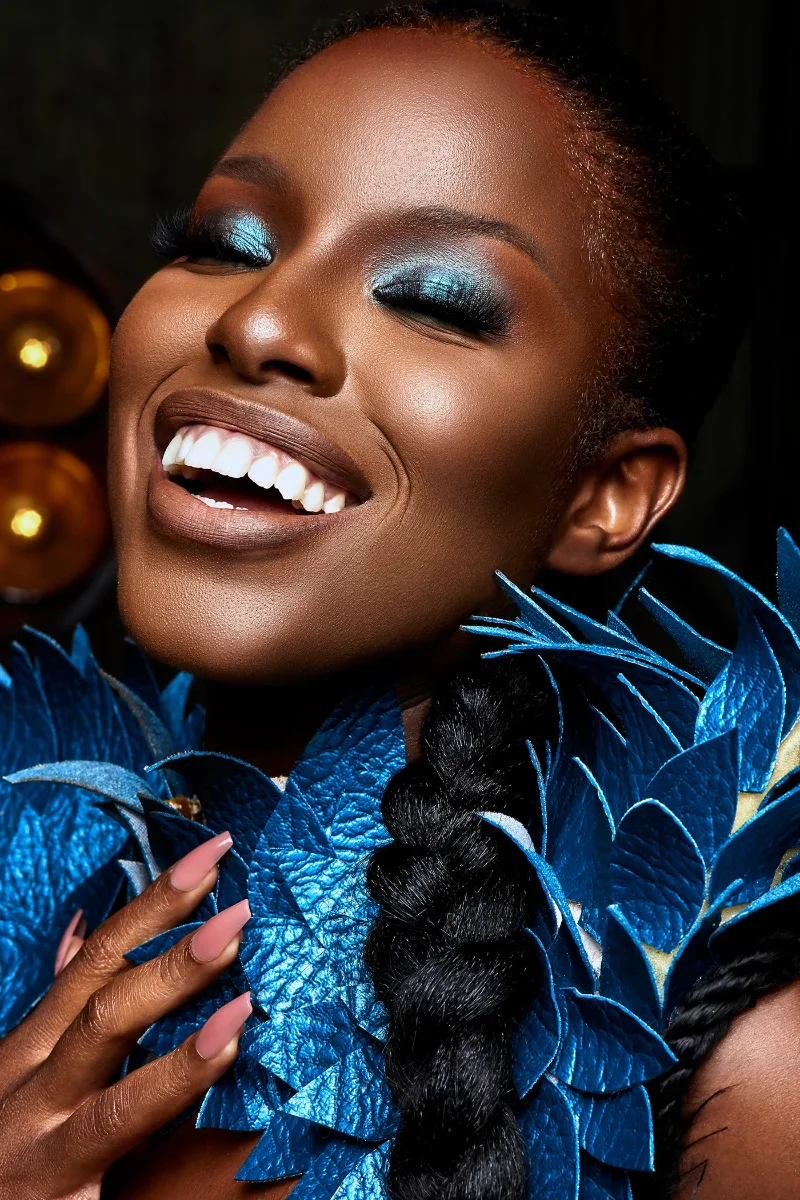 Creative fashion and beauty retouching showing a smiling Black model with metallic blue eyeshadow and an elaborate blue leaf collar